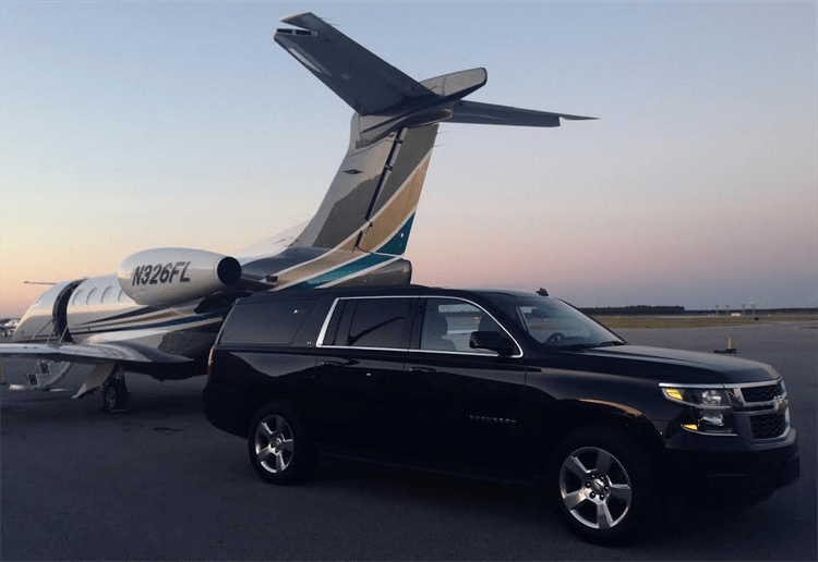 Black Chevrolet Suburban next to private jet at airport tarmac